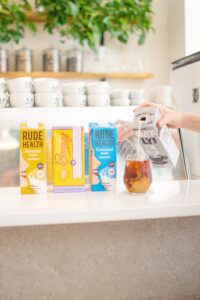 Almond, Soya and Coconut milk cartons in a row. Oat milk being poured into an iced coffee